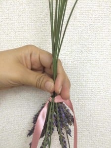 茎を2本下に折り曲げ、その下にリボンを通します。その少し右側に、また2本茎を折り曲げ、今度はリボンの下に茎がくるようにします。