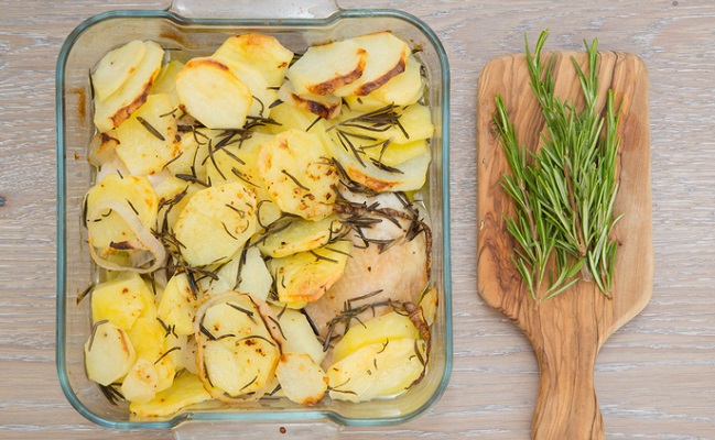 Baked potatoes with chicken, onion and rosemary in the glass mould and fresh rosemary on the cutting board.Top view